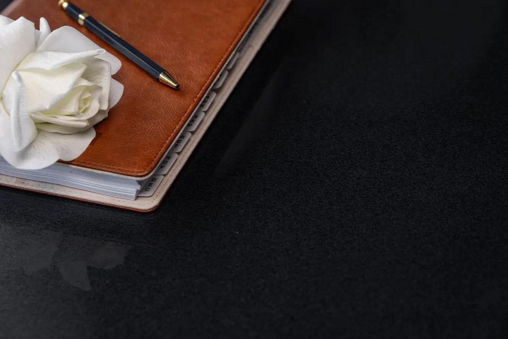 A Pen is Sitting on Top of a Notebook Next to a White Rose — Better Stone in Caloundra West, QLD