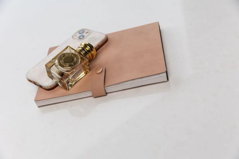 A Bottle of Perfume is Sitting on Top of a Notebook Next to a Cell Phone. — Better Stone in Caloundra West, QLD