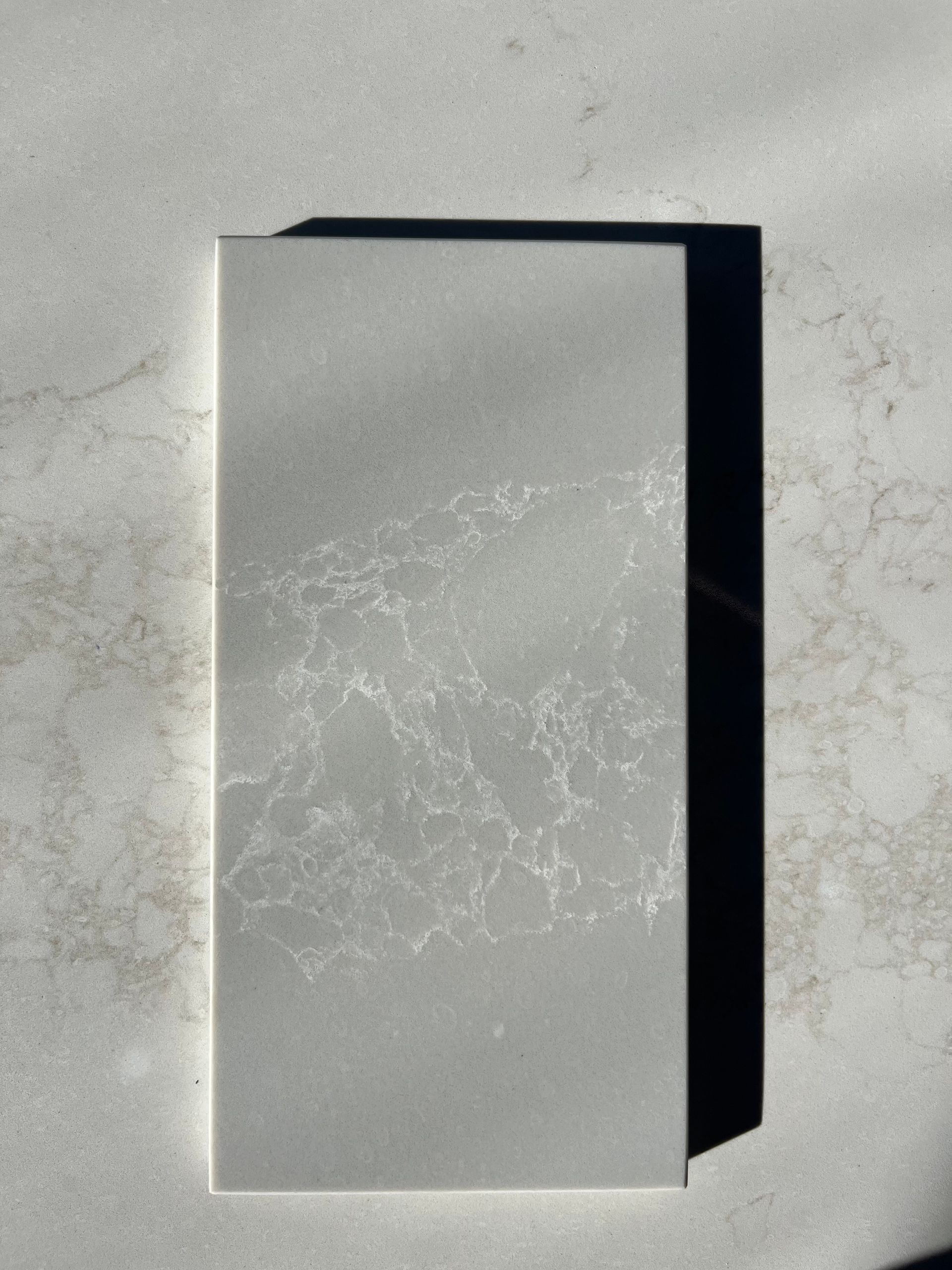 A rectangular gray stone tile with white veining, casting a shadow on a concrete surface.