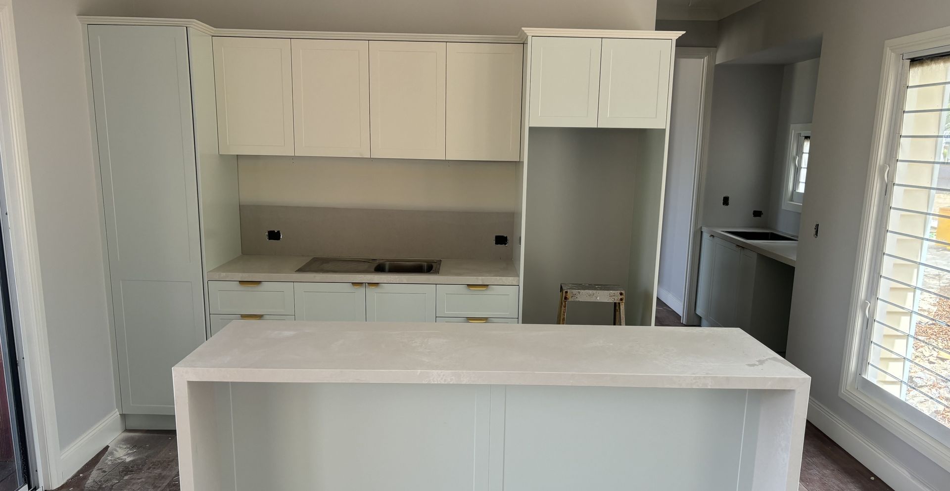 White kitchen cabinets with an island, in a room with a window and a partially built countertop.