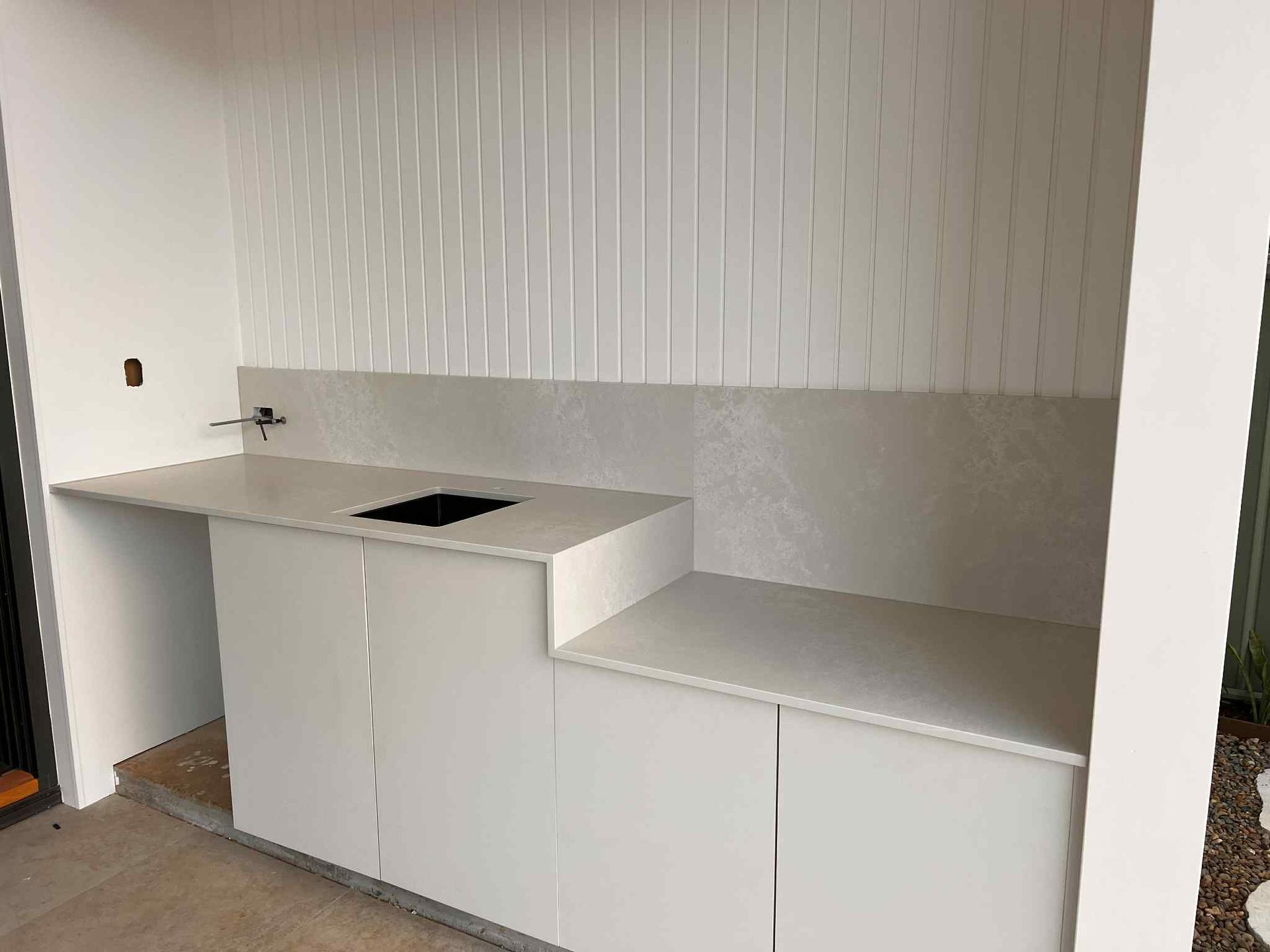 White Outdoor Kitchen With Countertop, Sink, and Cabinets Against a White Paneled Wall — Better Stone in Caloundra West, QLD