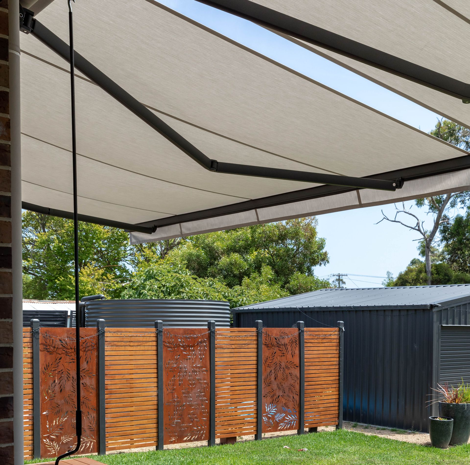 Retractable awning over a patio, with a decorative wooden fence and shed in the background.