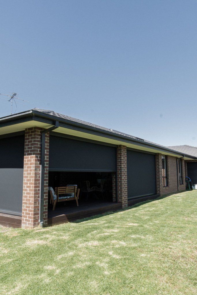 A home with brick columns and dark outdoor shades; a grassy lawn and clear blue sky.