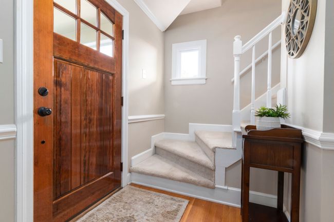 Front entry with wooden door, white staircase, and small table with plant in a bright hallway