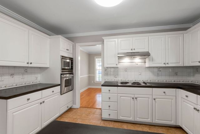 Bright white kitchen with black countertops, stainless appliances, and hardwood floor