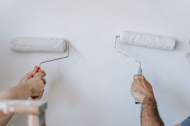 Two people rolling white paint on a wall with paint rollers