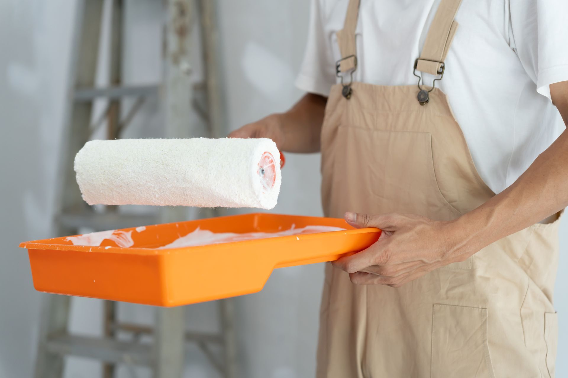 Person holding an orange paint tray with a white paint roller indoors