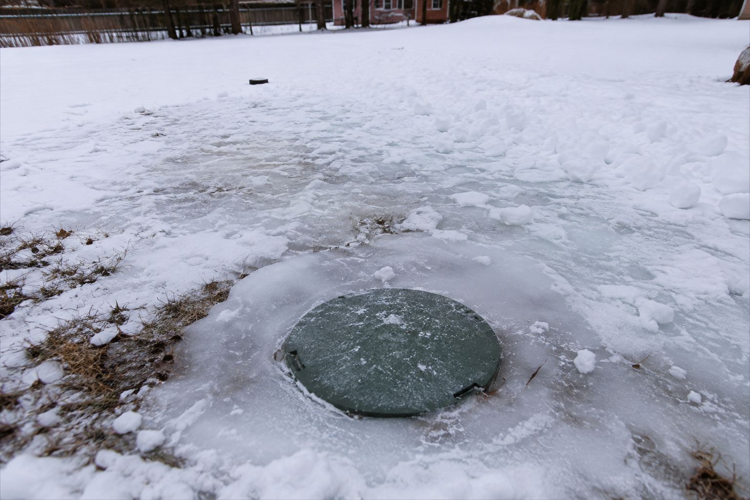Frozen pond with a circular green lid or cover embedded in the ice and snow-covered ground շուրջ