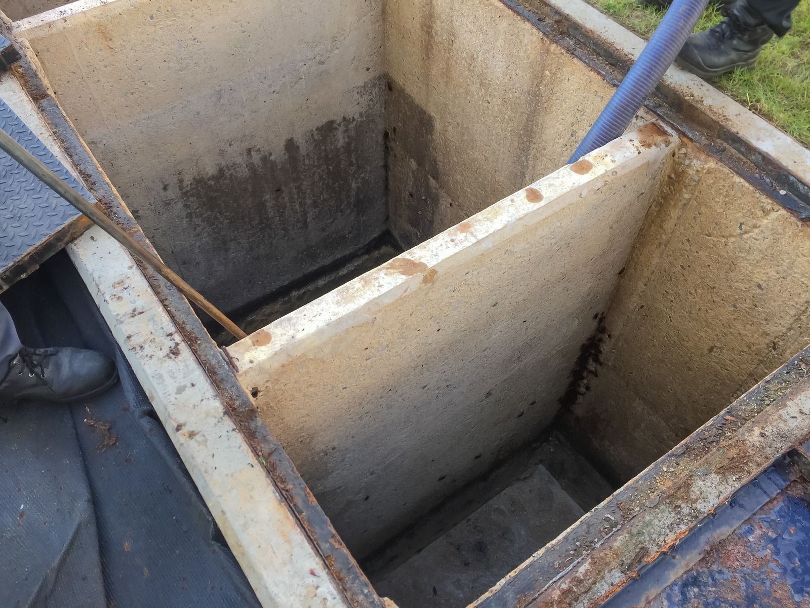 Open concrete utility pit with divided chambers and blue hose inside