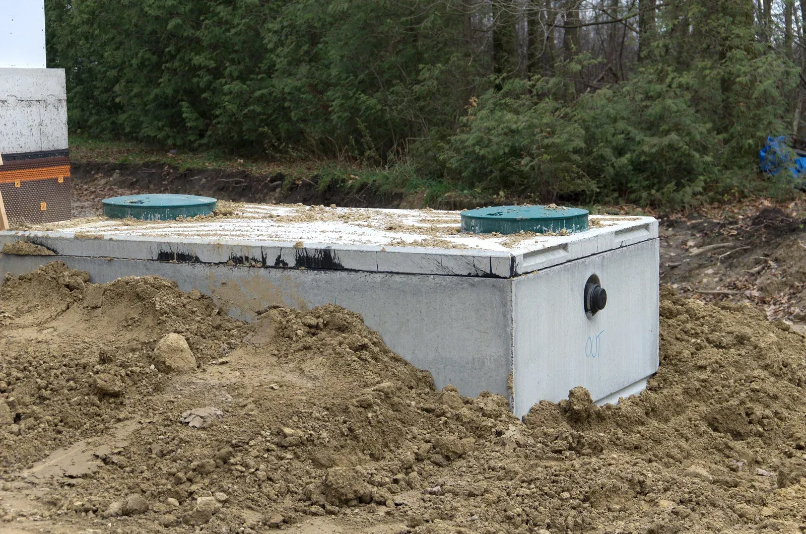 Concrete septic tank with two green lids, surrounded by dirt and vegetation.