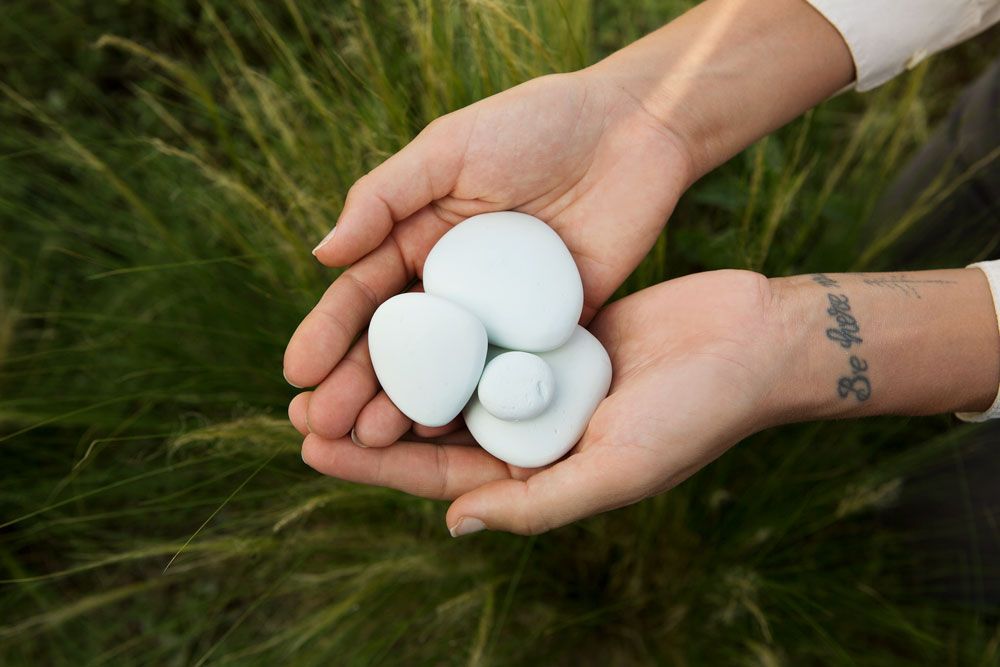 A person holding parting stoens in their hands above a field of grass
