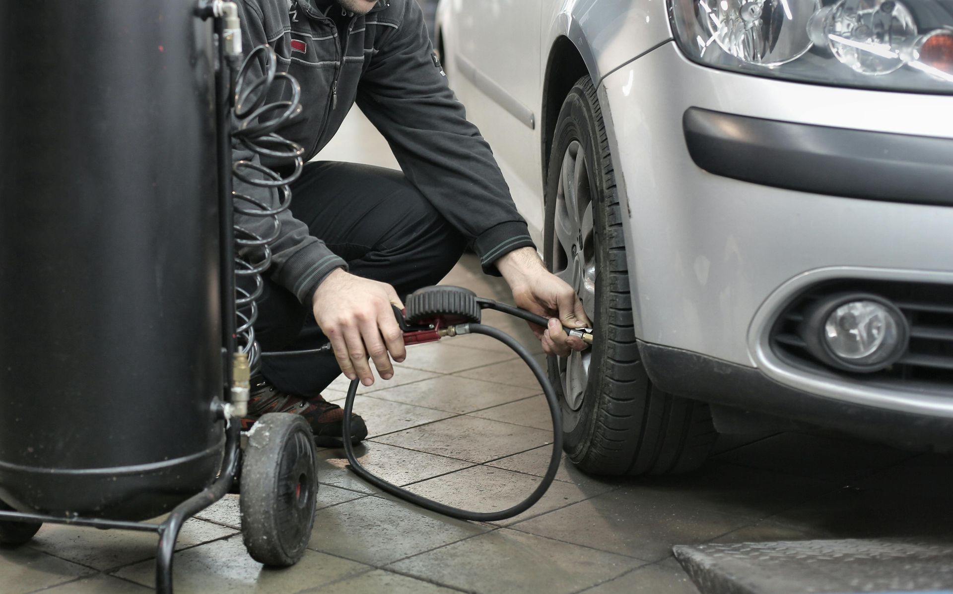 Mechanic inflating a car tire in a garage with an air compressor.