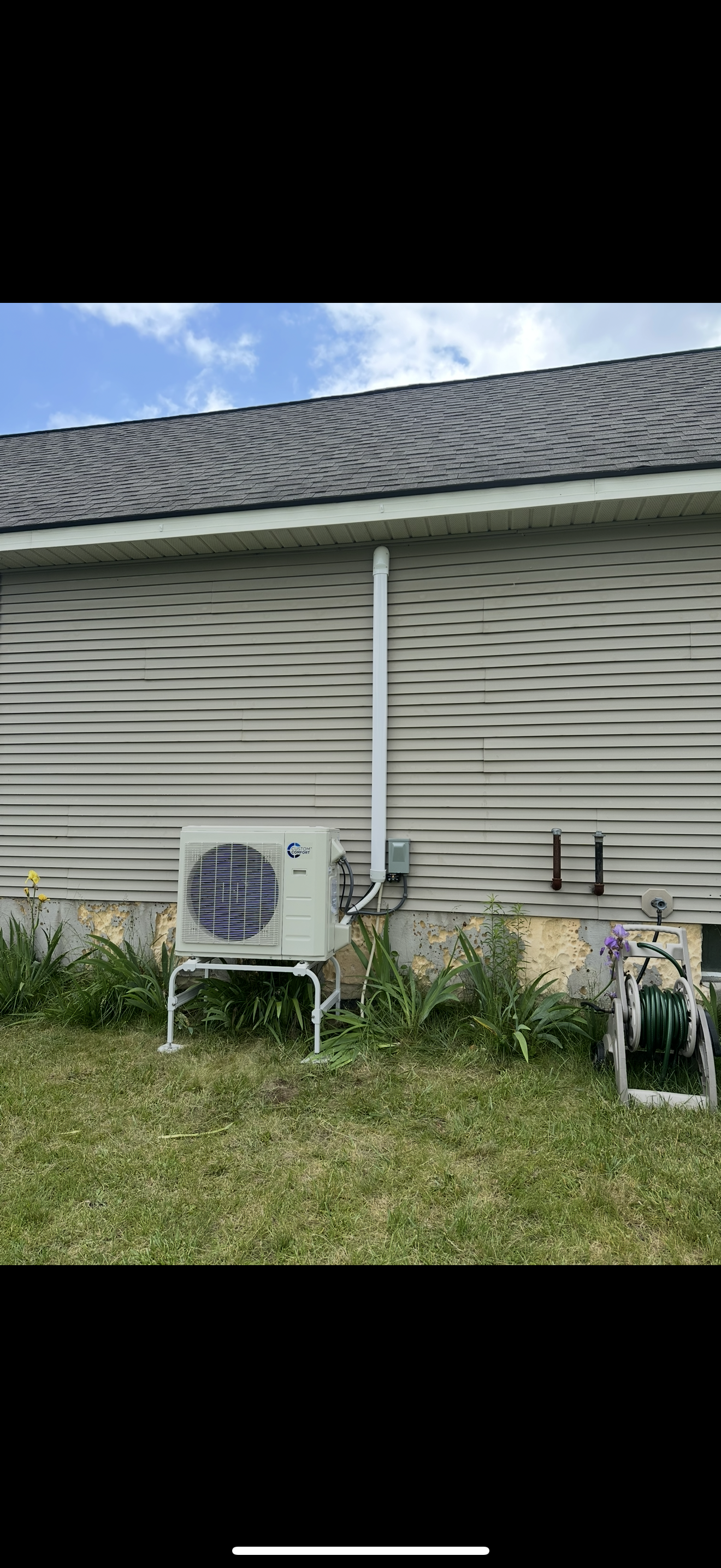 Outdoor HVAC unit beside a beige house with white siding and a shingled roof, surrounded by grass.