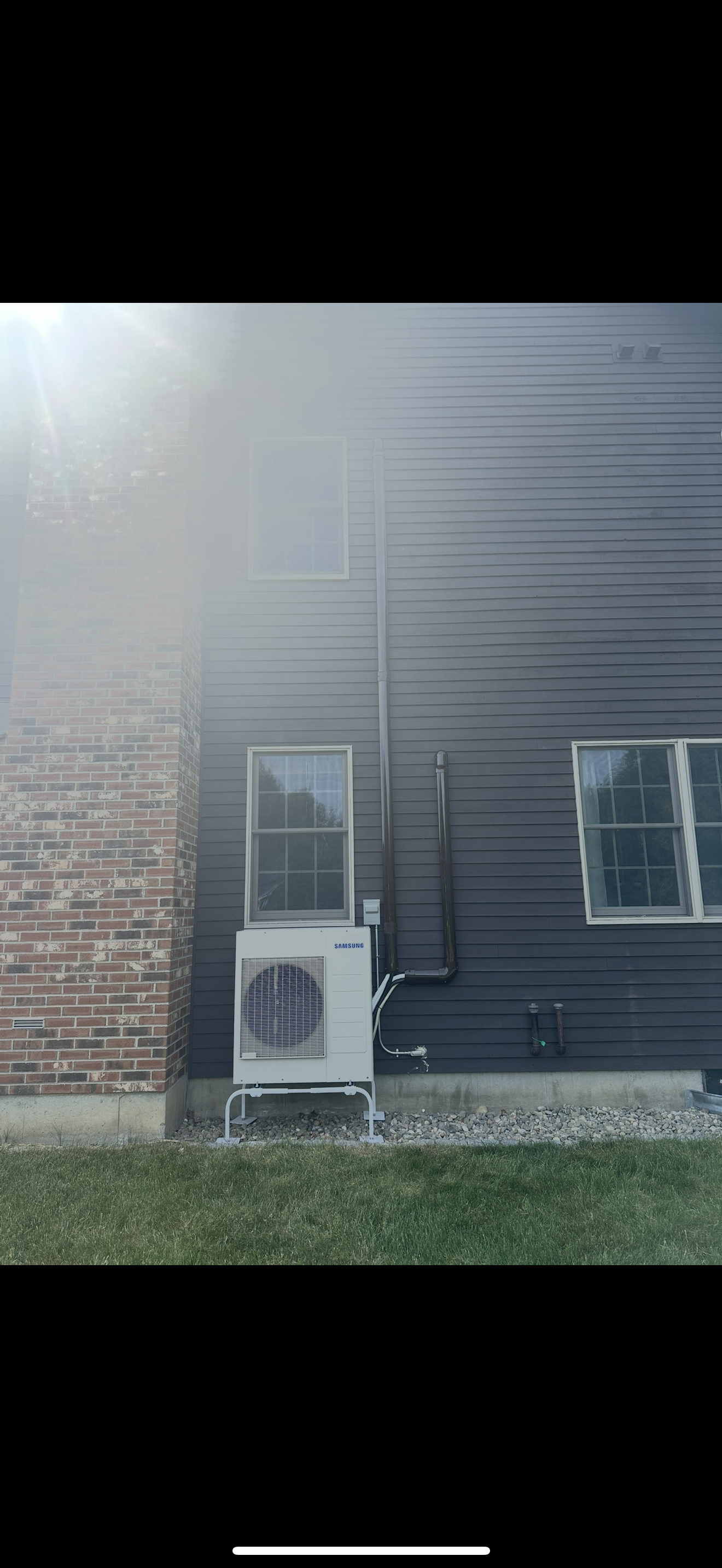 Air conditioner units beside a dark house wall and brick exterior in a grassy yard.