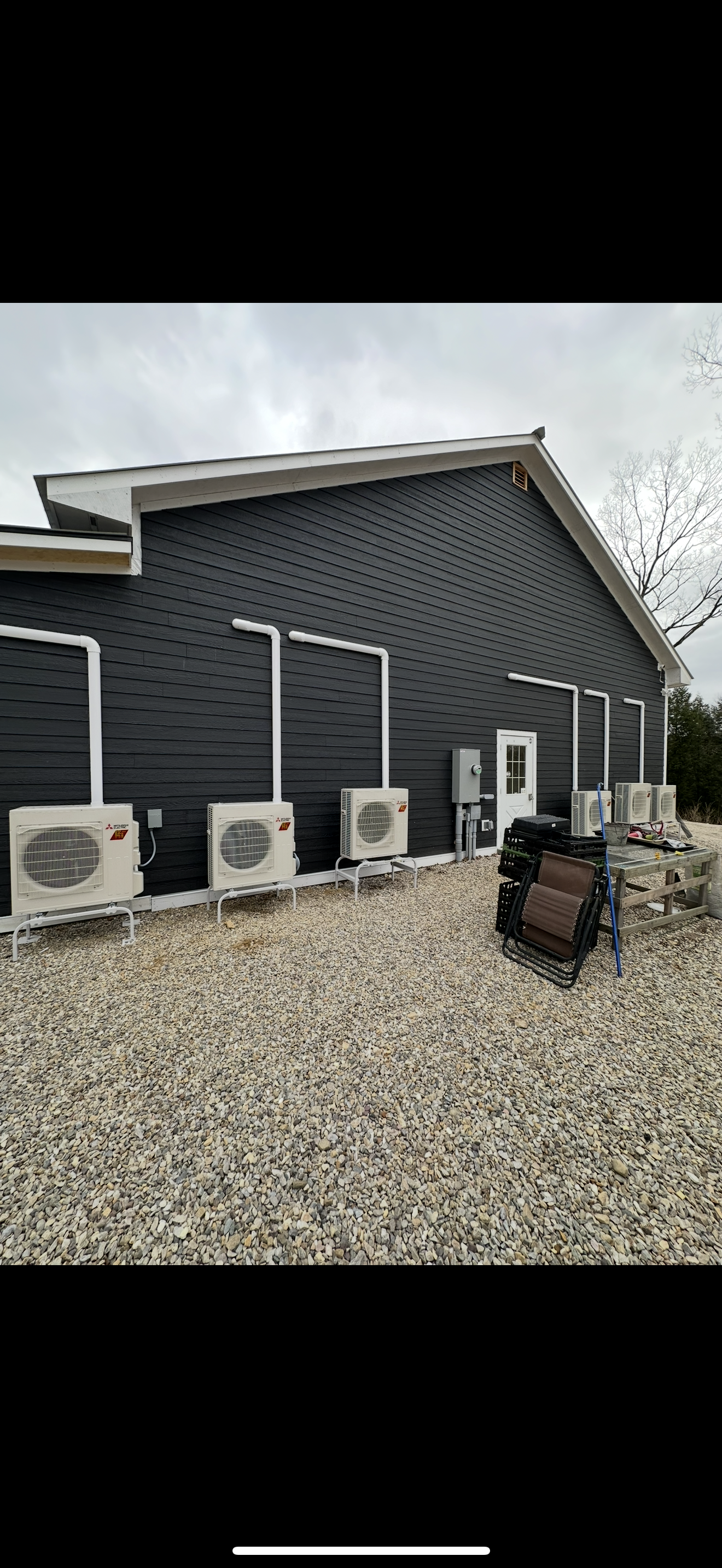 Gravel yard beside a dark gray building with several white air-conditioning units and a gate.