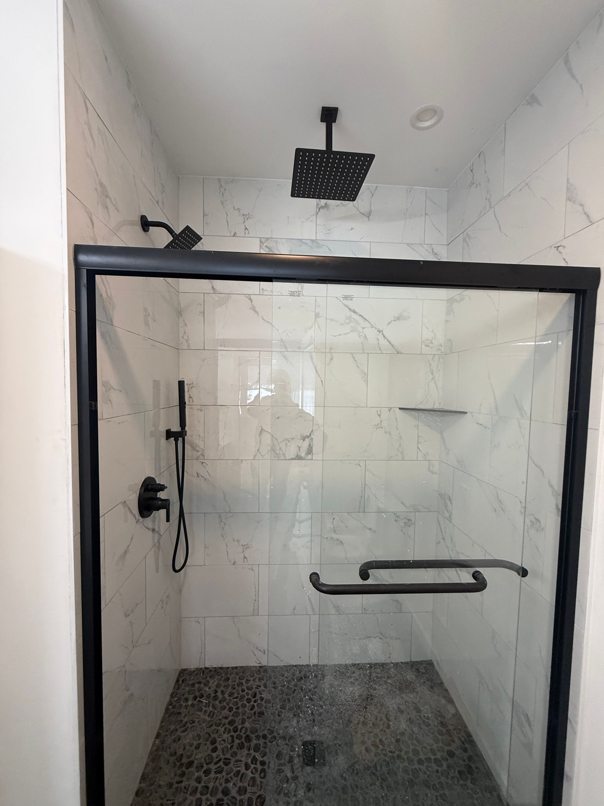 Glass-enclosed shower with white tile walls, dark stone floor, and black shower fixtures.