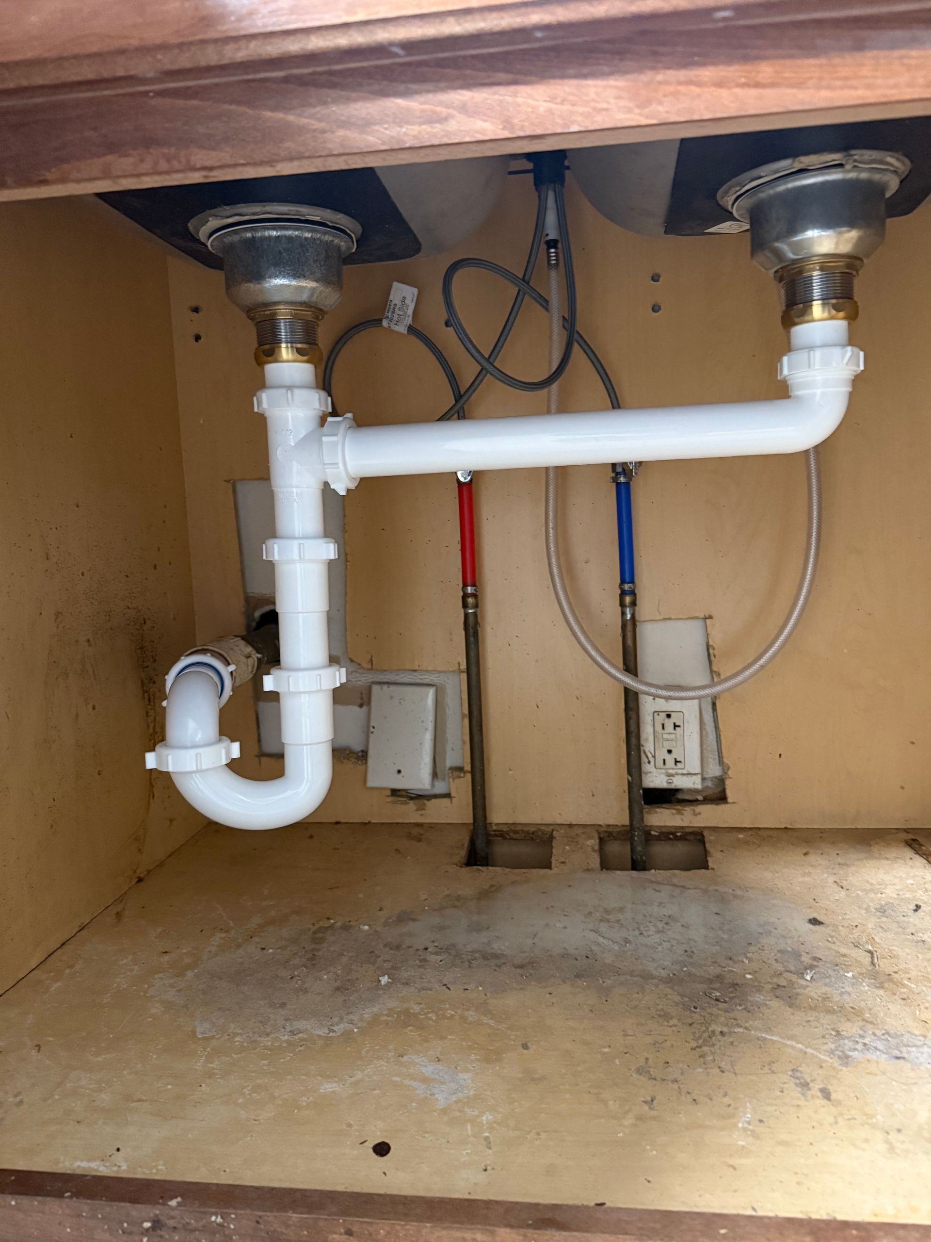 Under-sink plumbing with white PVC pipes and drain lines in a cabinet opening