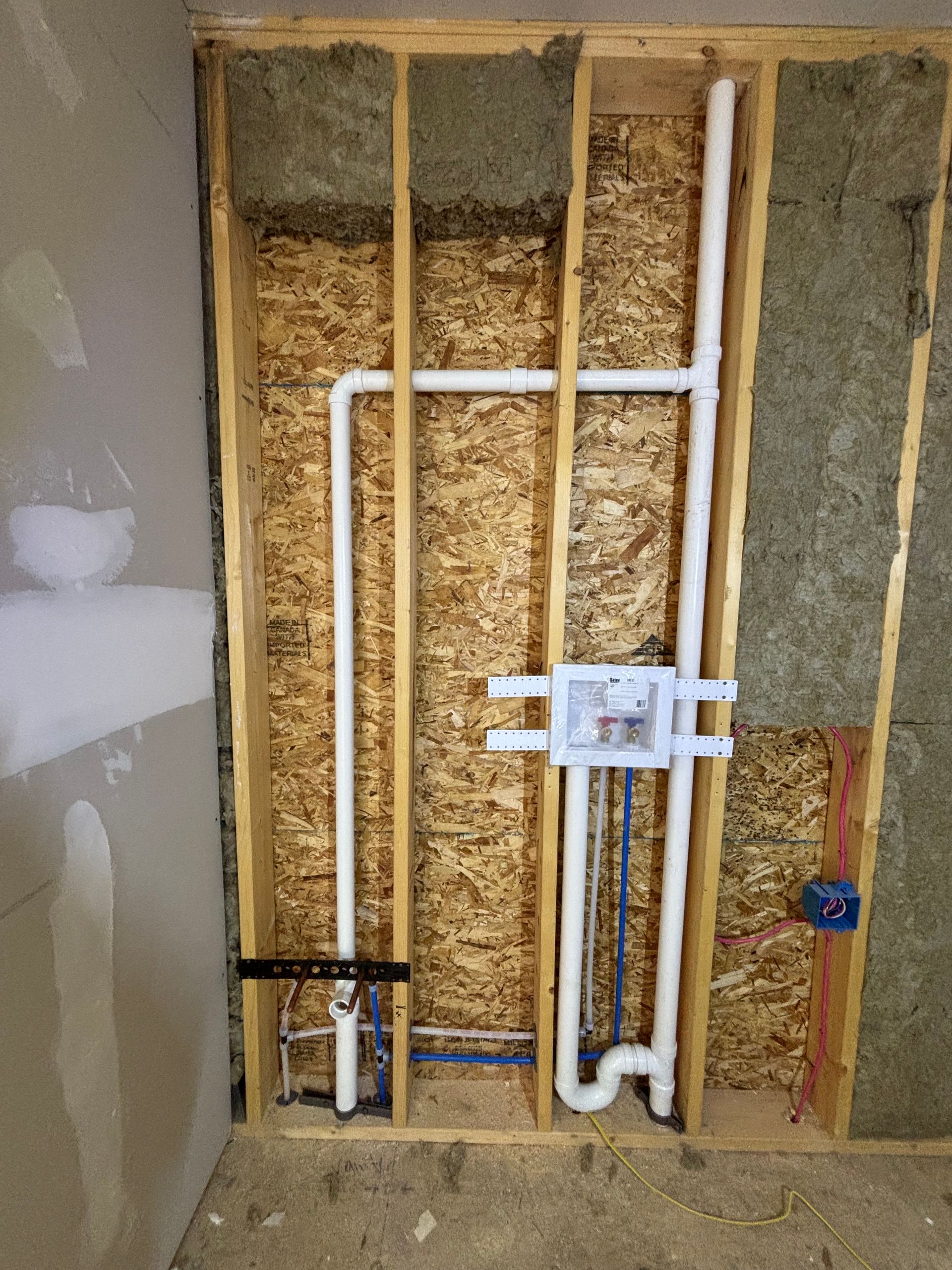 Unfinished bathroom wall with exposed insulation and plumbing pipes for a shower fixture