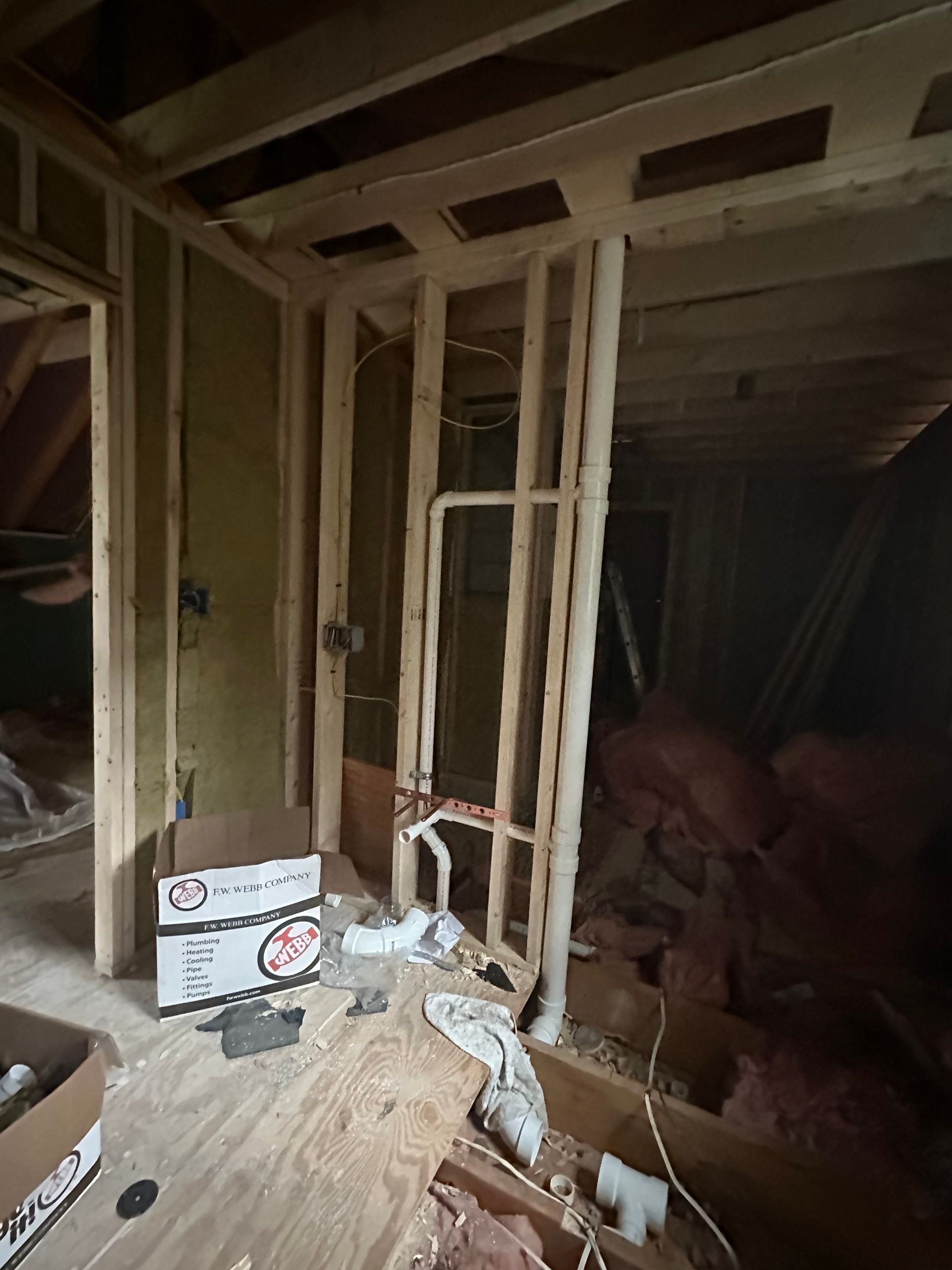 Partially constructed room with exposed wooden framing, drywall, and construction debris on the floor.