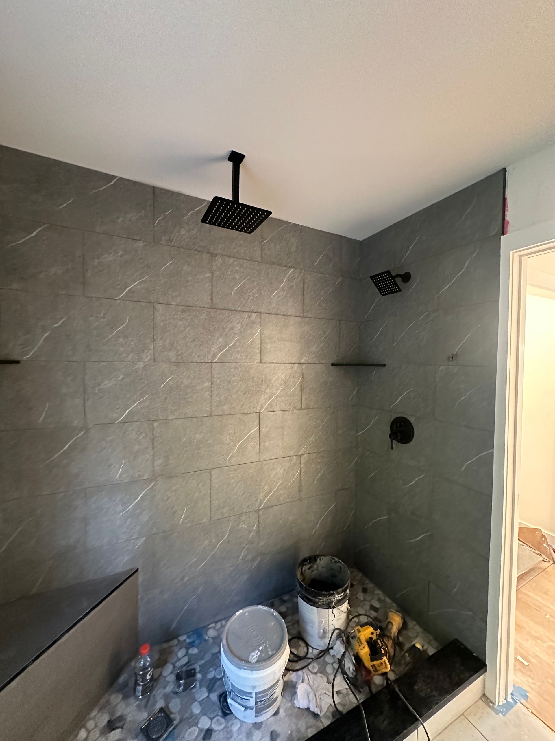 Partially finished bathroom with gray tile, exposed fixtures, and paint cans on the floor