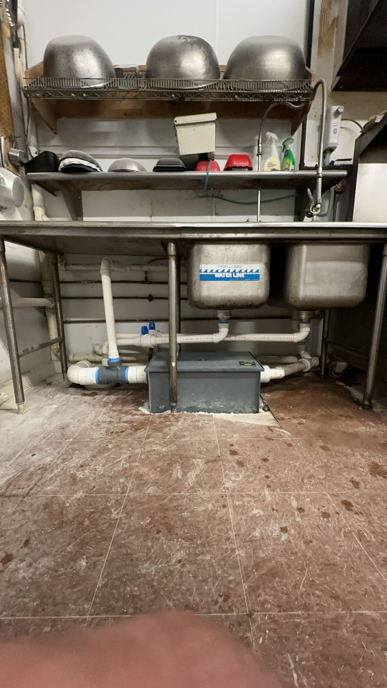 Industrial kitchen sink area with stacked stainless steel bowls, shelves, and a wet floor.