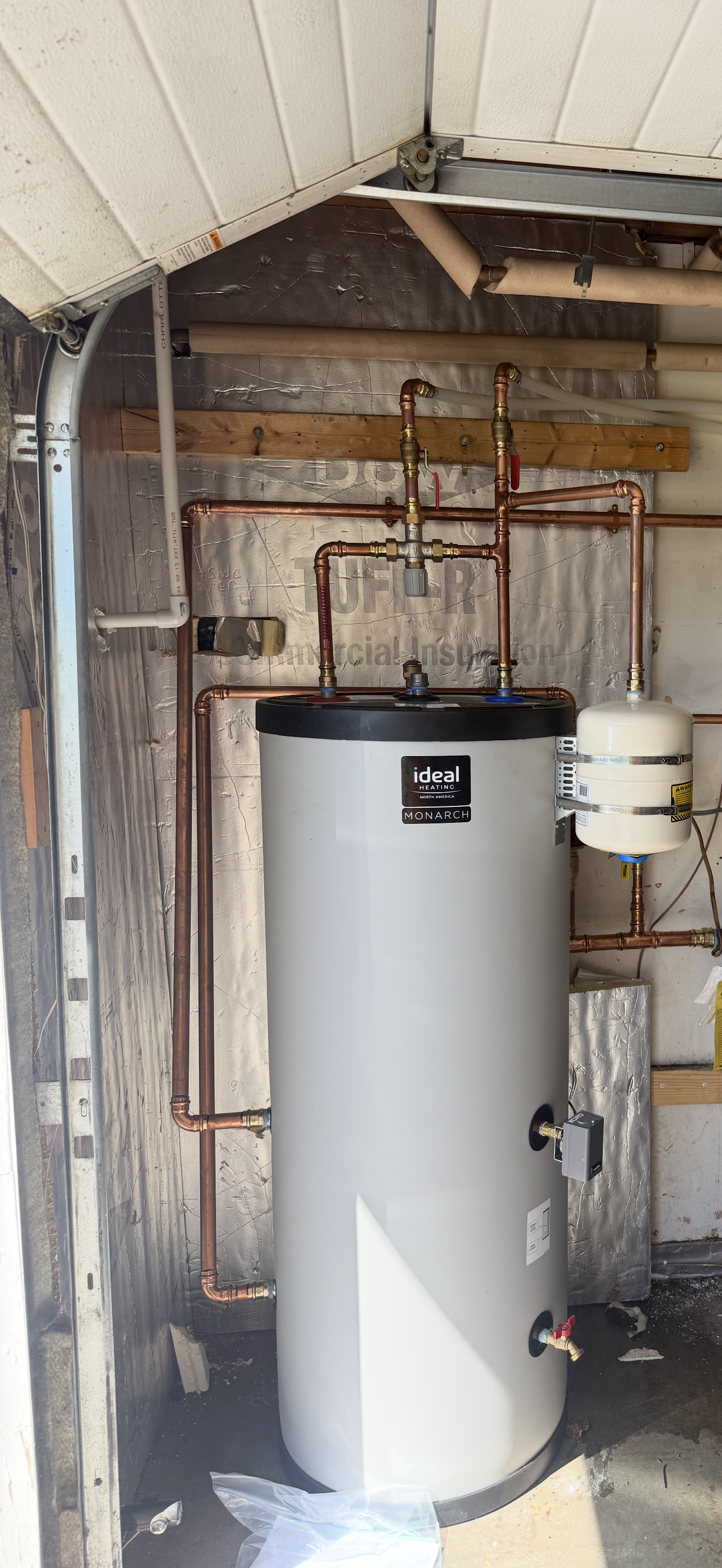 Water heater and exposed plumbing in a narrow utility closet beneath a slanted roof.