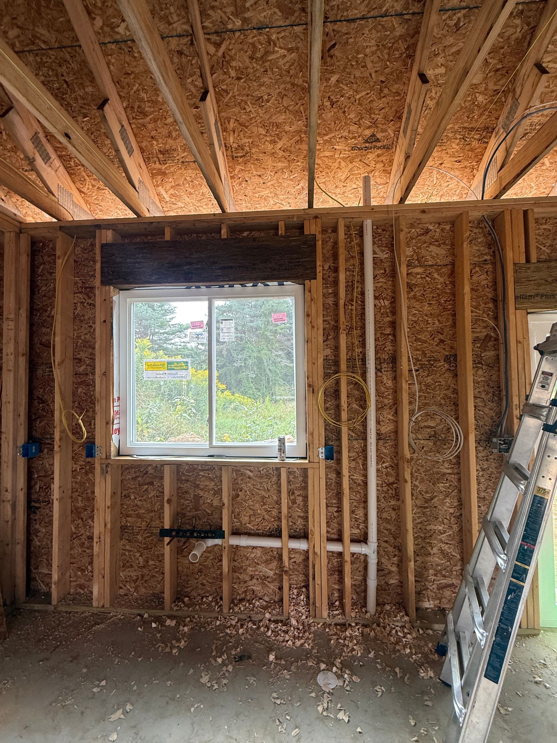 Exposed wall framing in a house under construction, with a window and insulation visible.