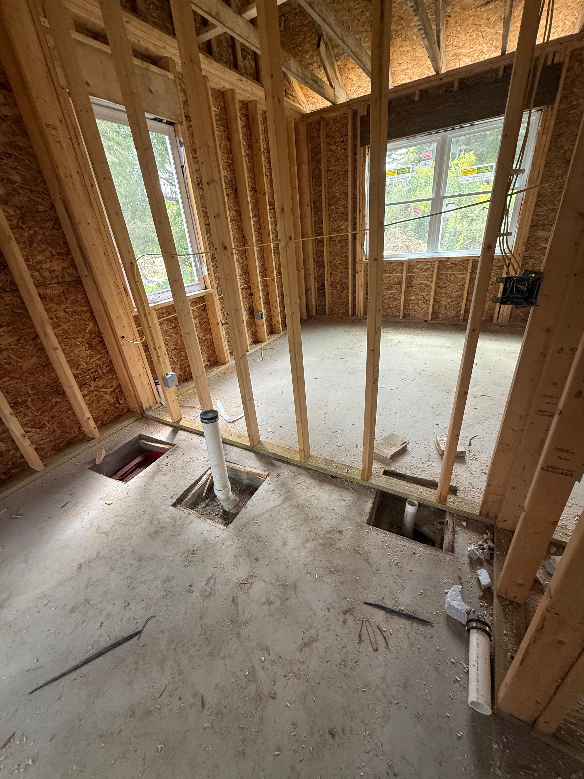 Unfinished room framed with exposed studs, concrete floor, and windows letting in daylight.