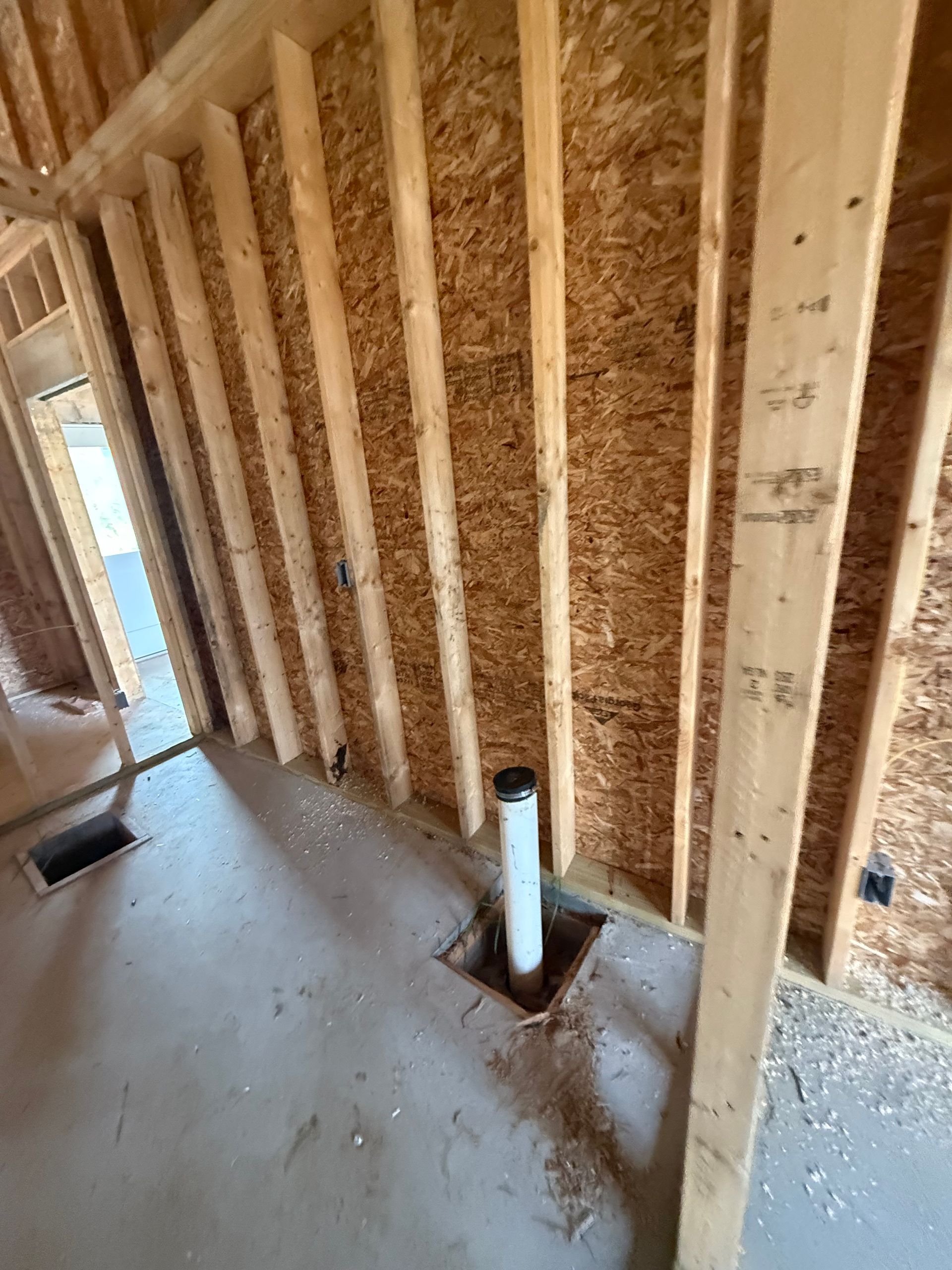Framed interior wall with exposed studs, insulation, and a floor drain pipe opening
