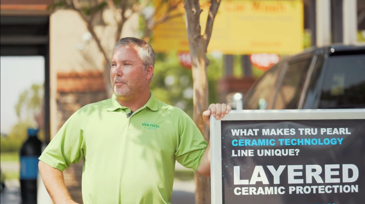 A man in a green shirt is holding a sign that says layered ceramic protection
