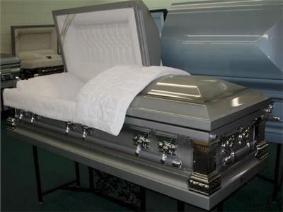 Silver casket with open lid, white interior bedding, displayed on a table.