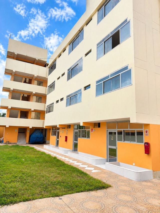 Moderno edificio de apartamentos con paredes naranjas y beige, balcones y un patio con césped bajo un cielo azul