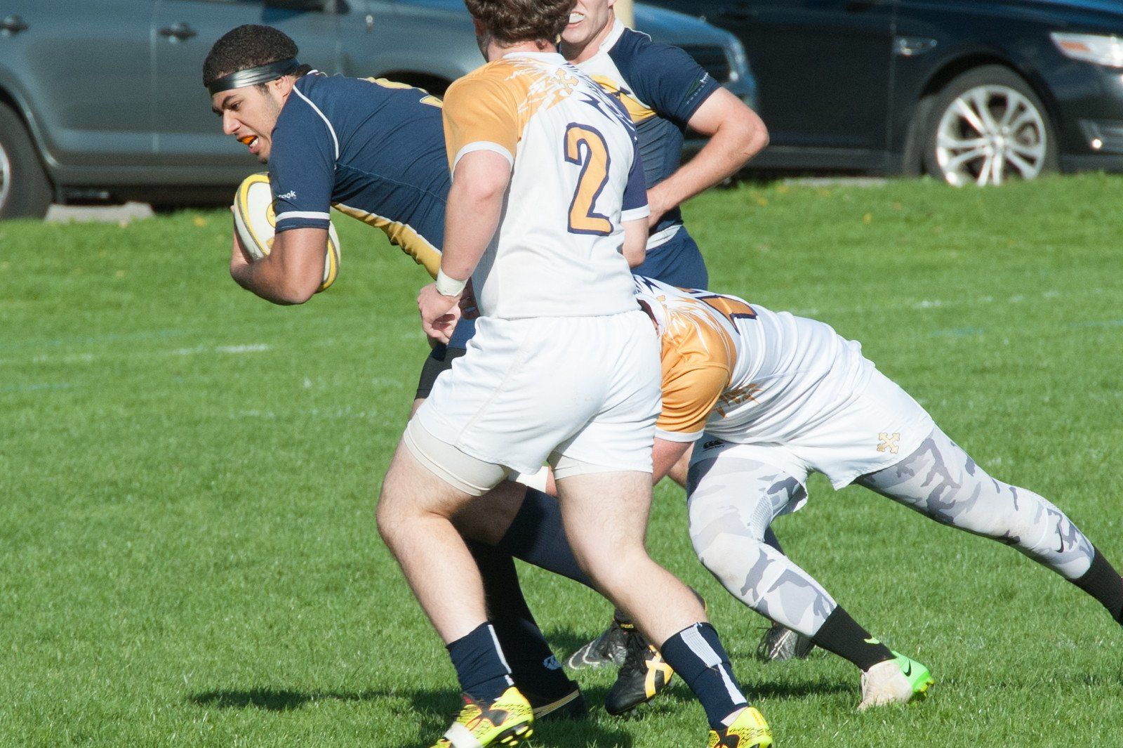 A rugby player with the number 2 on his jersey is being tackled by another player