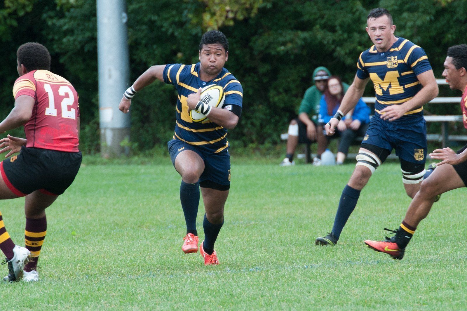 A rugby player with the number 12 on his jersey is running with the ball