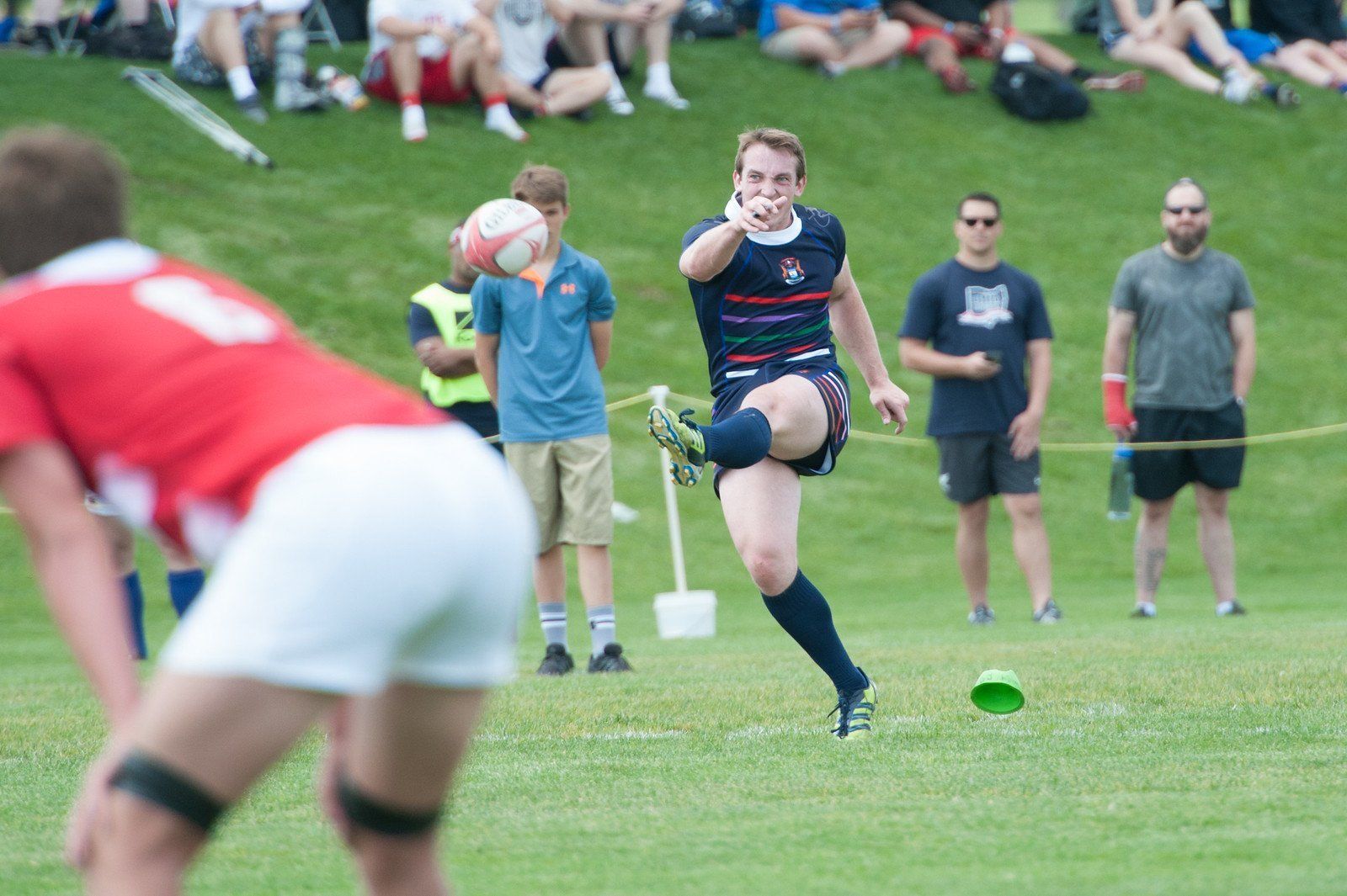 A man is kicking a rugby ball while another man watches.