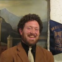 A man in a suit and tie is smiling in front of a painting.