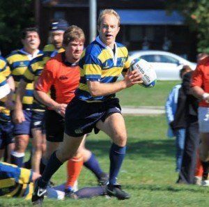 A man in a blue and yellow striped shirt is running with a rugby ball