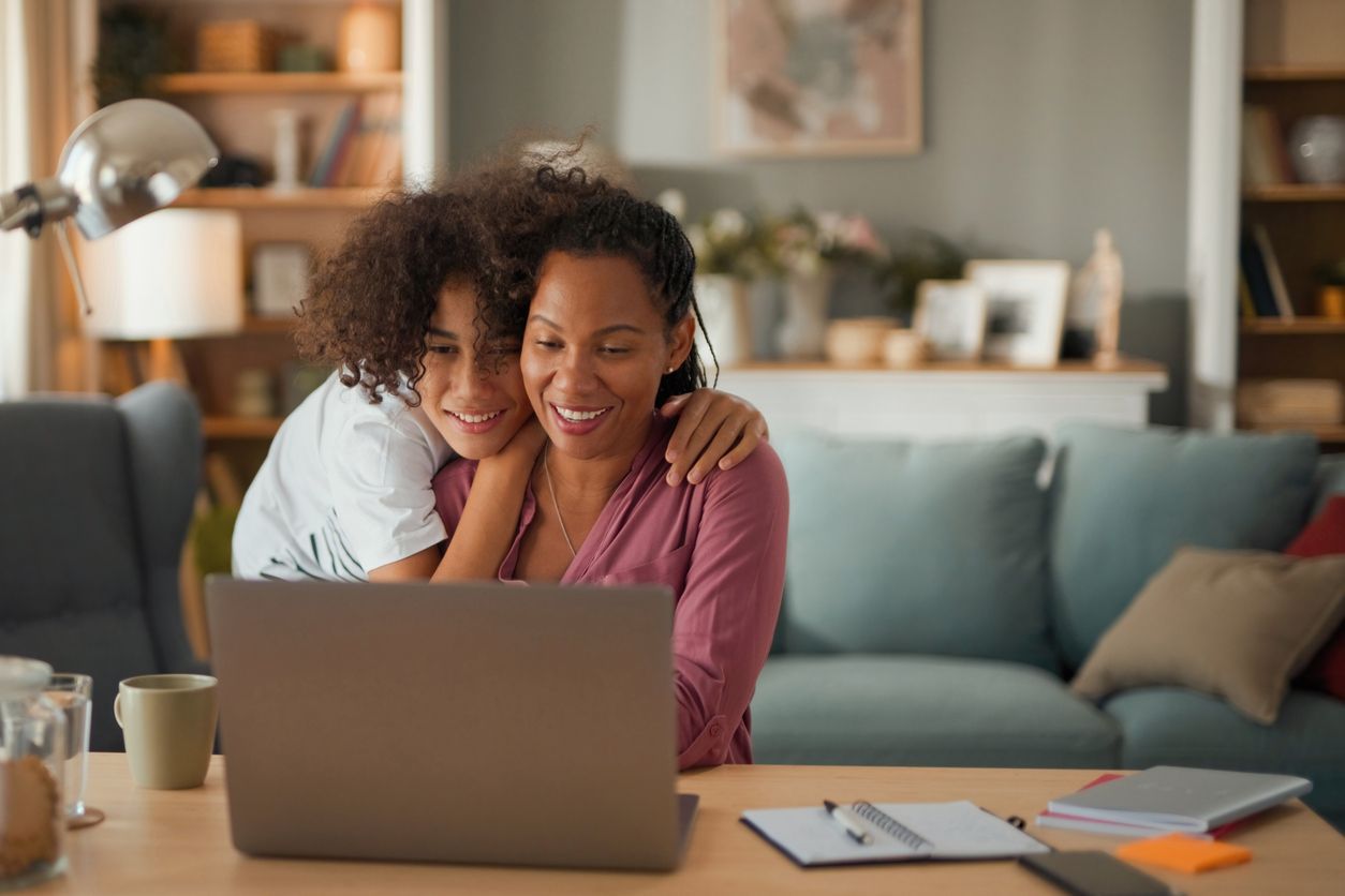 A woman and a child are sitting at a table looking at a laptop computer.