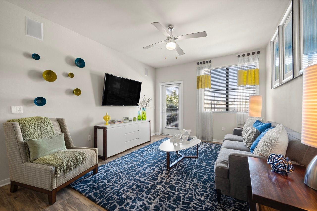 Modern living room in an apartment with a gray sofa, accent chair, wall TV, and a blue rug.