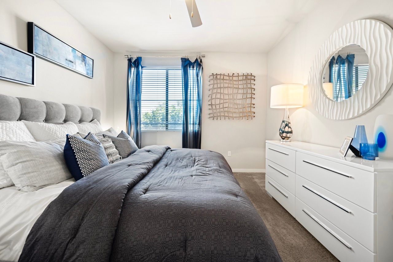 Bedroom in apartment with a large bed, white dresser, round mirror, and blue accents.