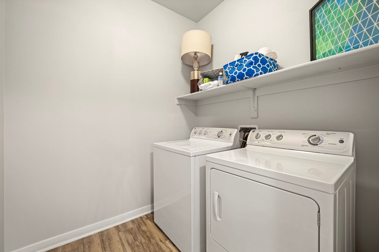 White washer and dryer in a small laundry closet with a shelf and decor items.
