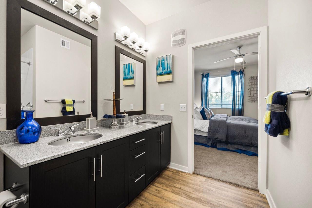 Dual-sink bathroom with granite countertops and a doorway to the bedroom.