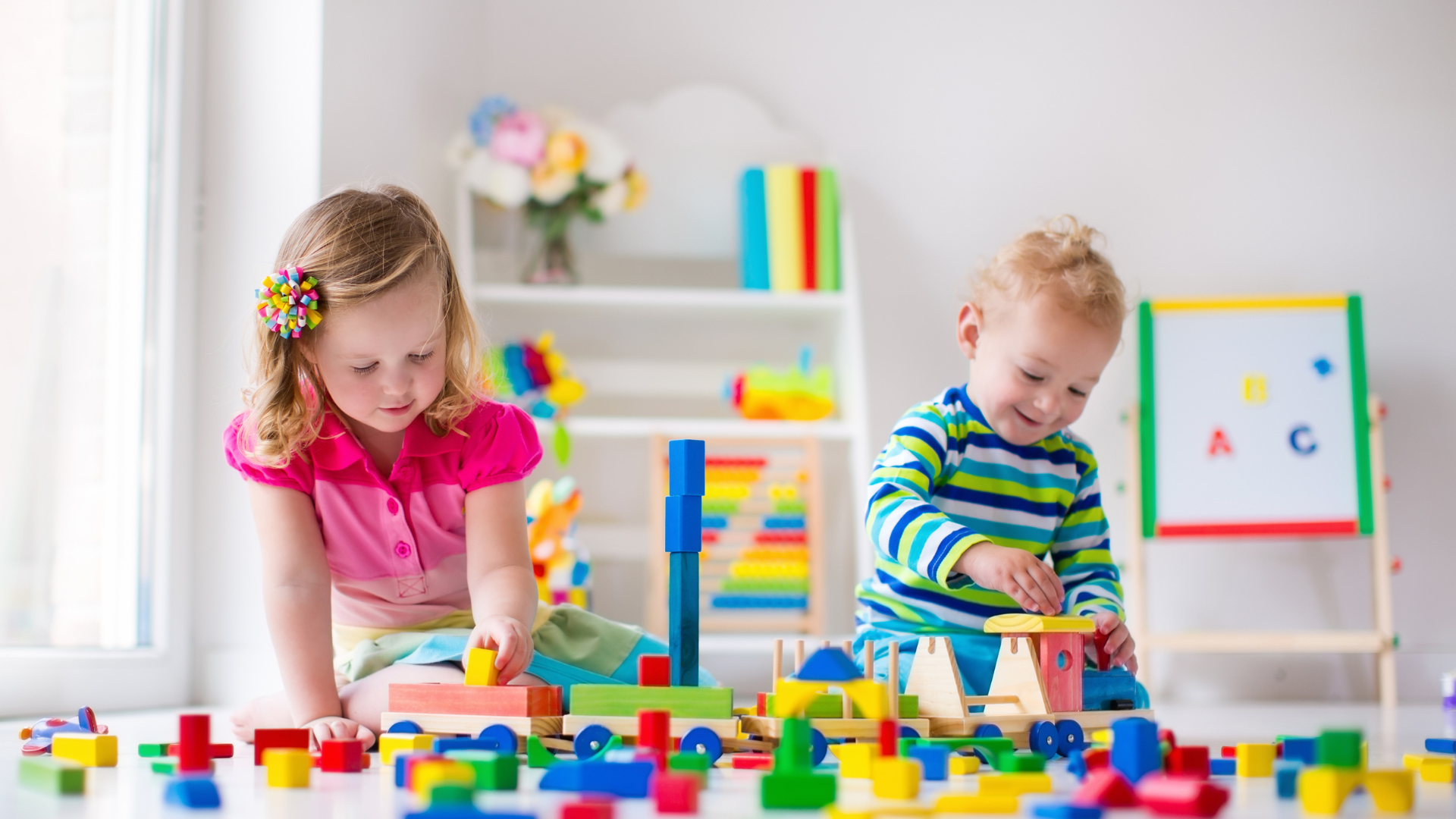 Two young children playing with colorful building blocks in a bright room.