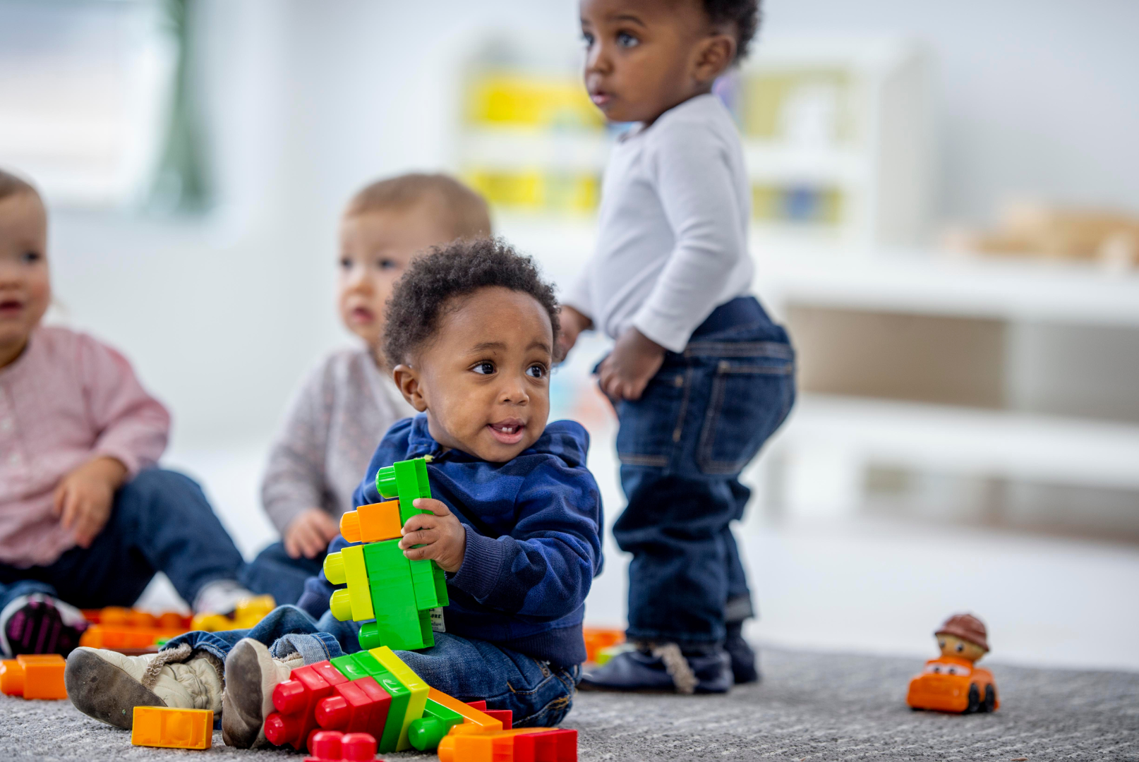 Woman sitting with two babies playing with toys in a classroom setting.
