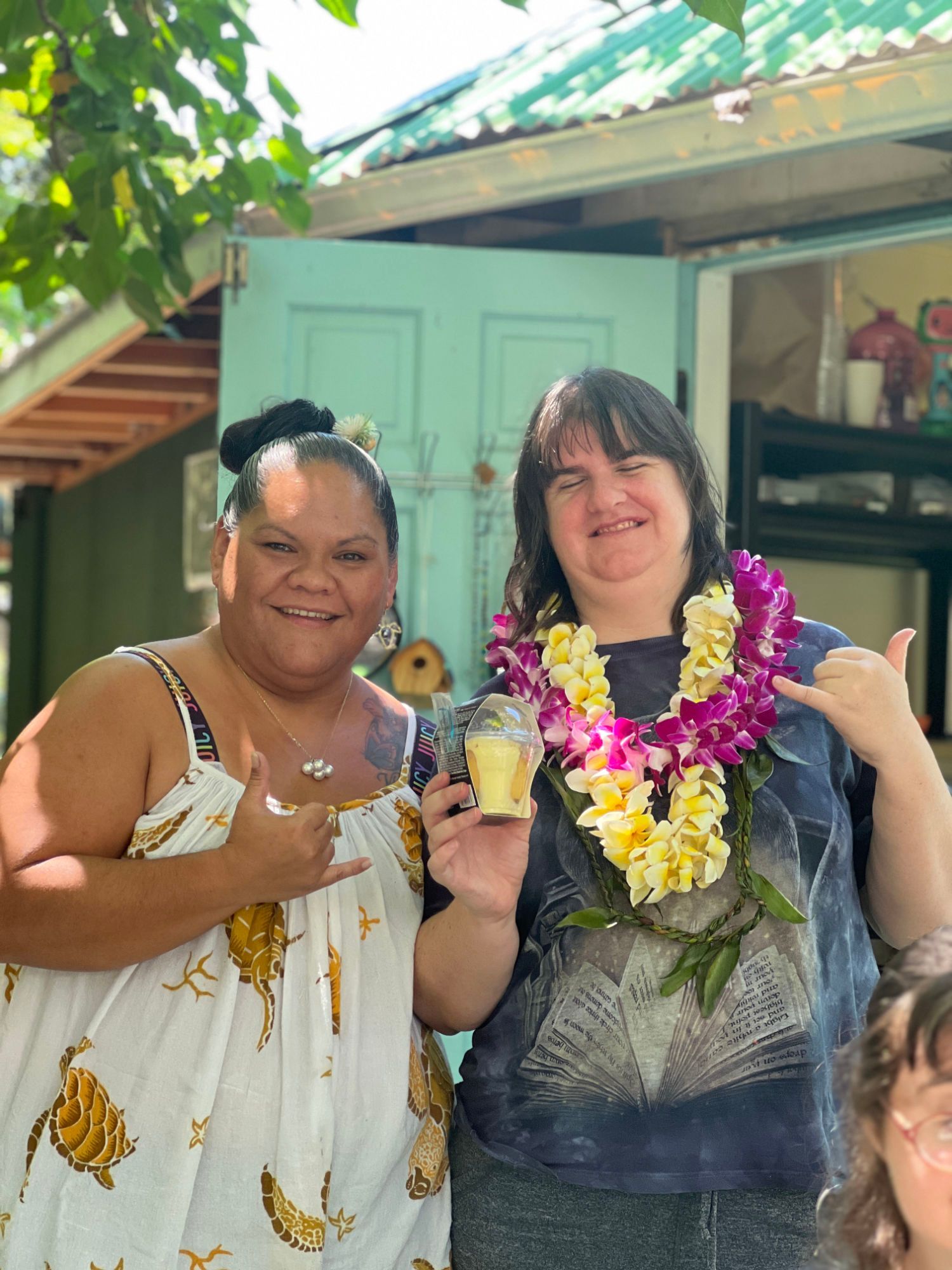 Two women are posing for a picture in front of a house . one of the women is wearing a lei.