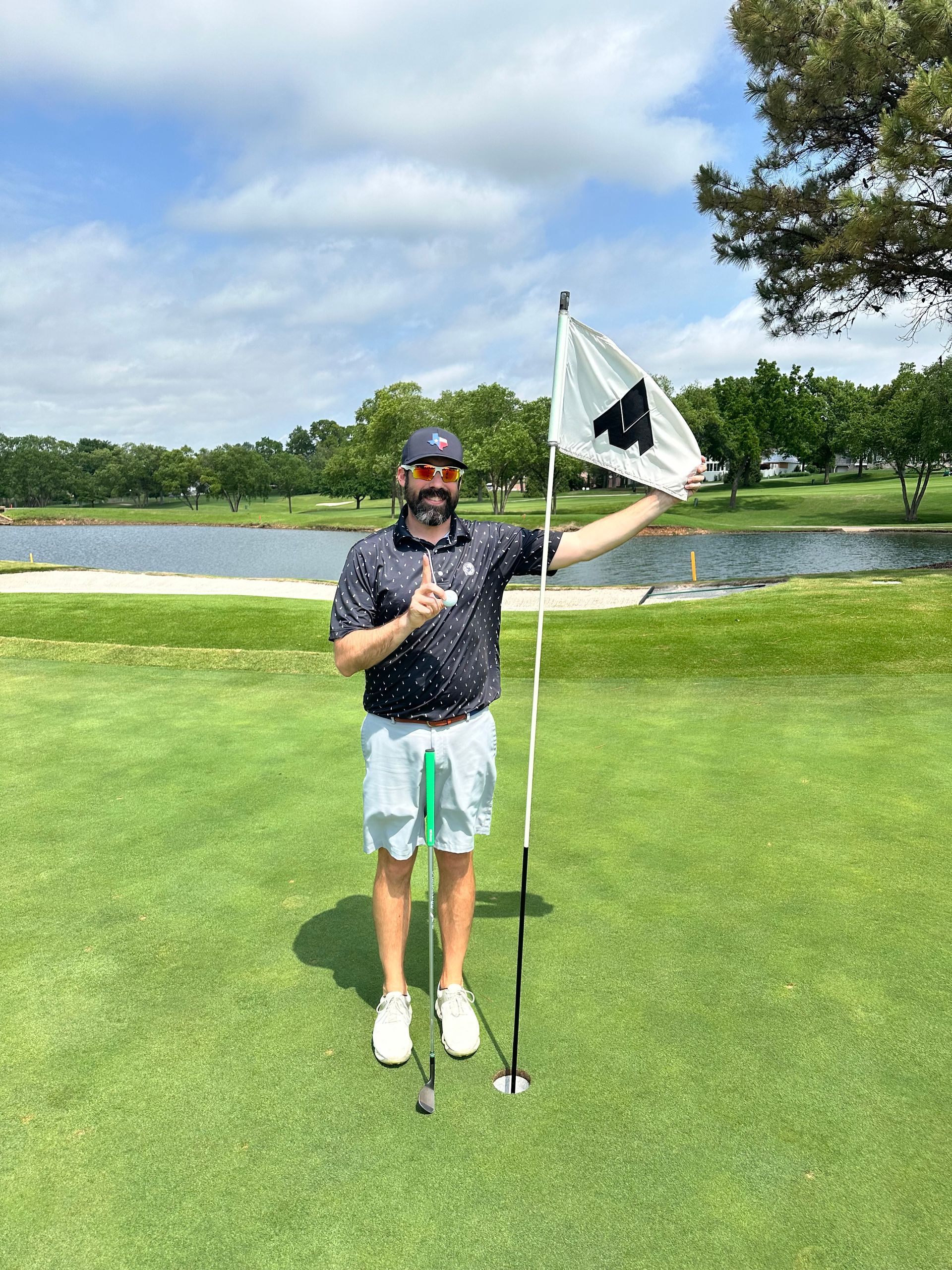 A man is standing on a golf course holding a flag and giving a thumbs up.