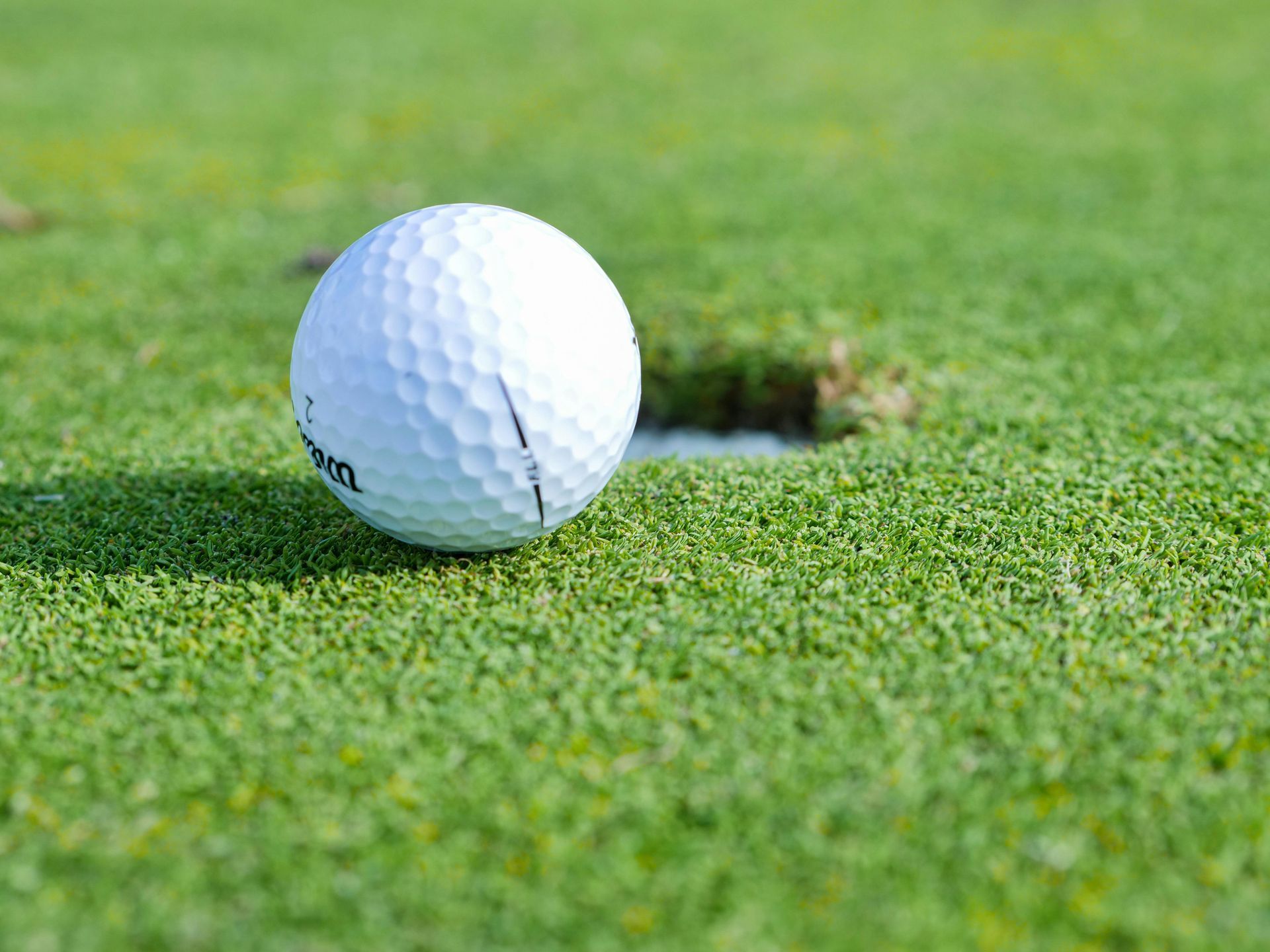 A golf ball is sitting on the edge of a hole on a golf course.