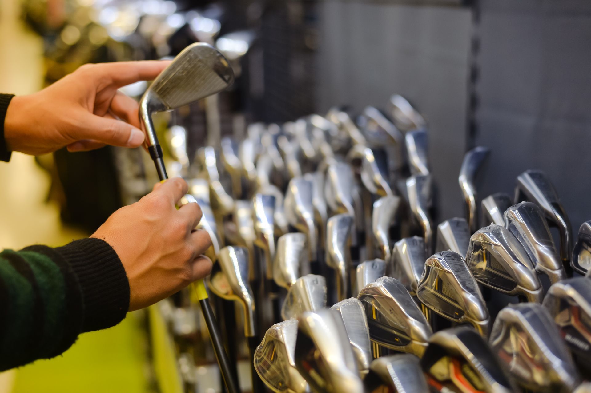 A person is holding a golf club in front of a row of golf clubs.