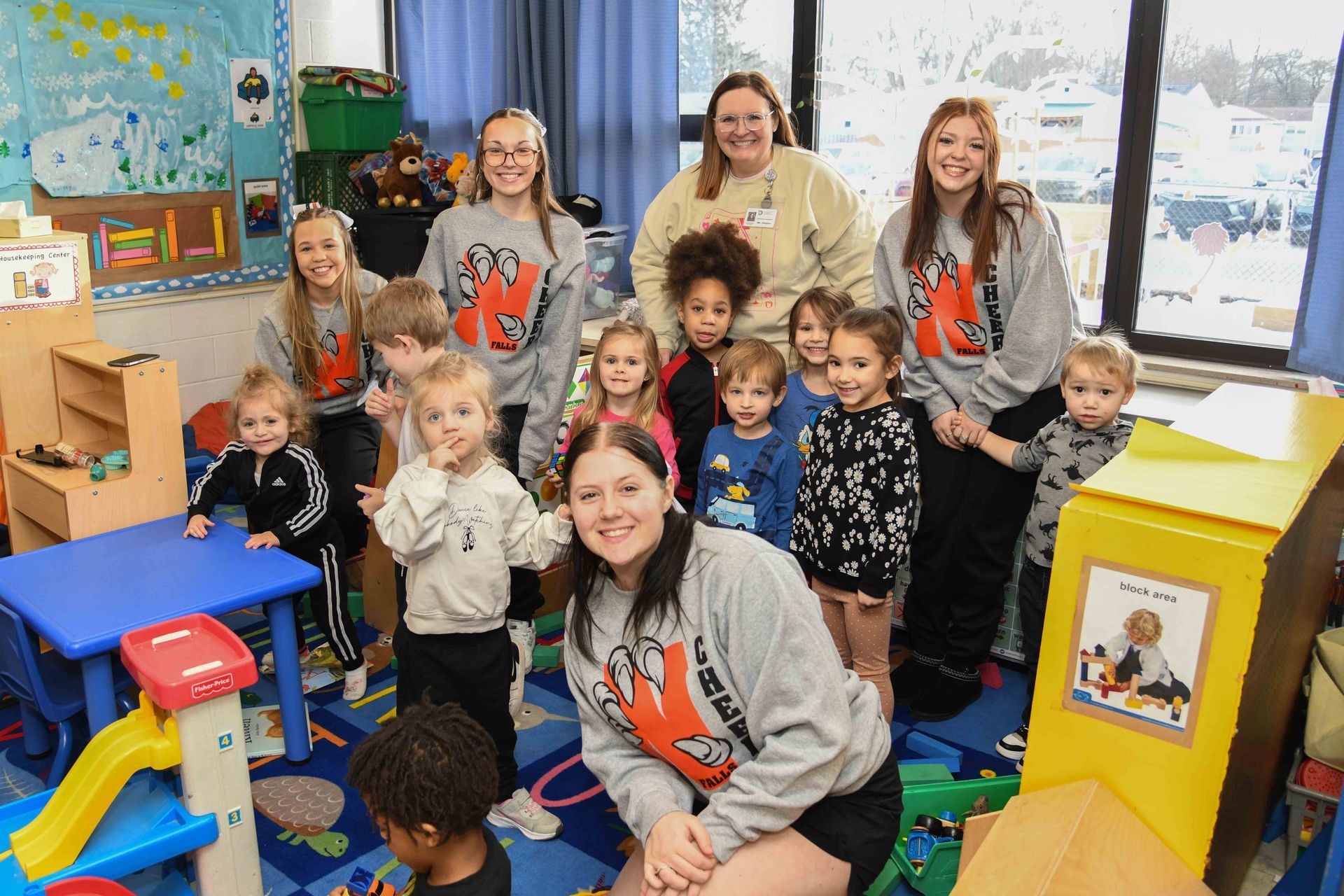 Group of children and adults in a colorful playroom, smiling and posing for a photo.