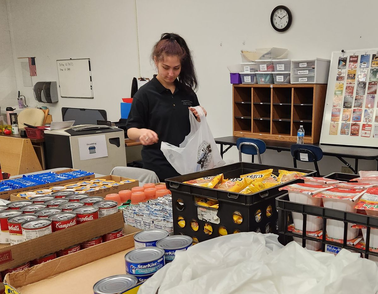 Woman filling a bag with food items at a food bank, surrounded by organized donations.